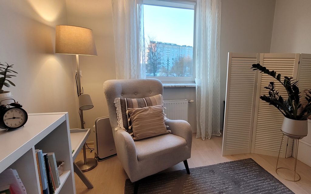 zdjęcie gabinetu przedstawiające wygodny fotel z poduszkami, obok lampa stojąca, roślina oraz dywan